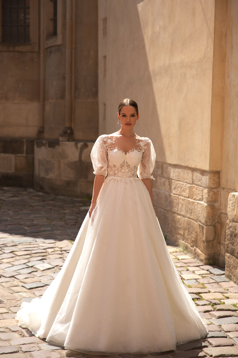 Ivory A-line wedding dress with a sparkling skirt, sheer puff sleeves, lace bodice, and court train