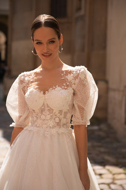 Close-up of a wedding dress bodice with floral lace, sparkling beadwork, sweetheart neckline, and sheer puff sleeves