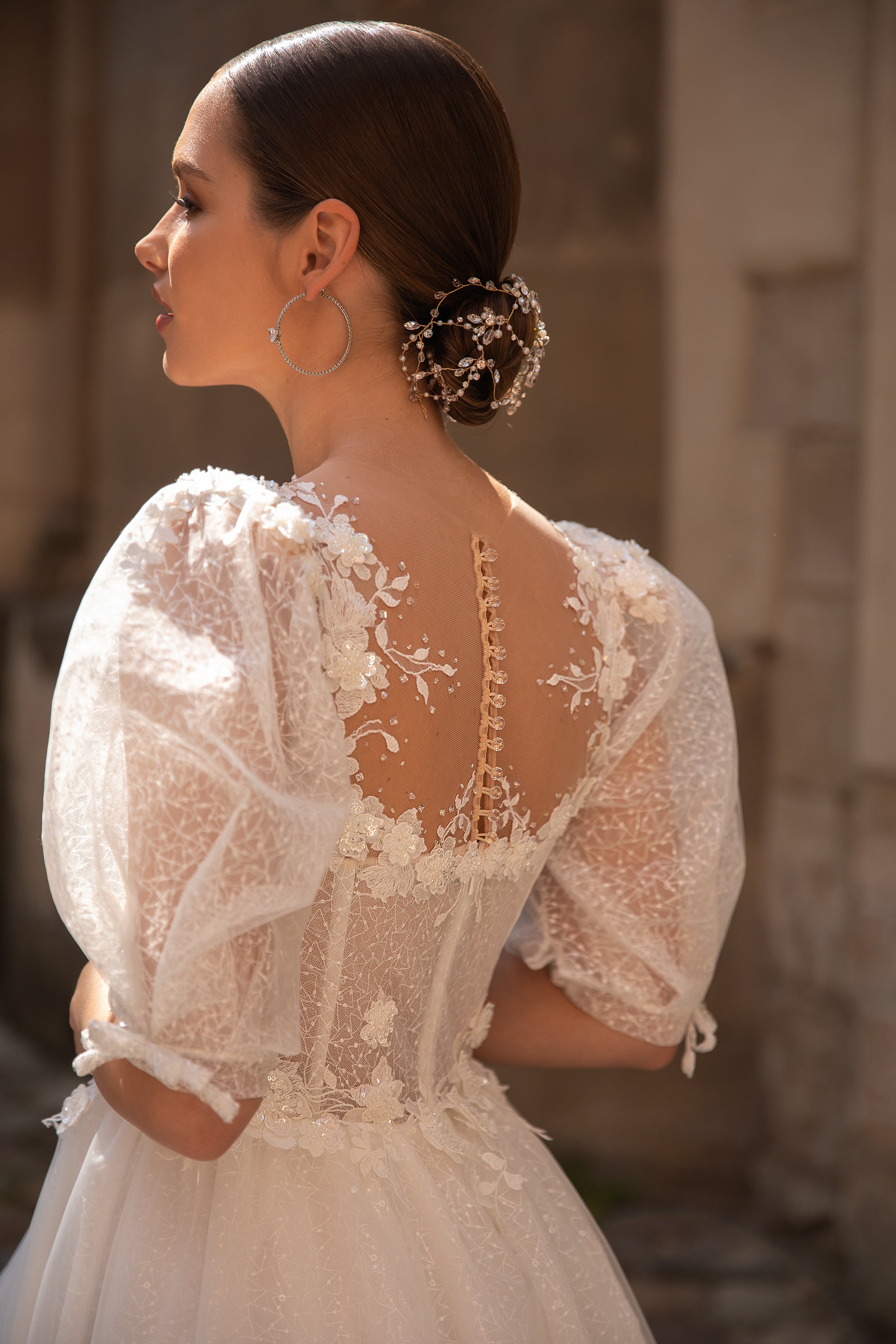 Open illusion-lace back on an ivory wedding dress with a button closure, floral appliqués, and sheer puff sleeves