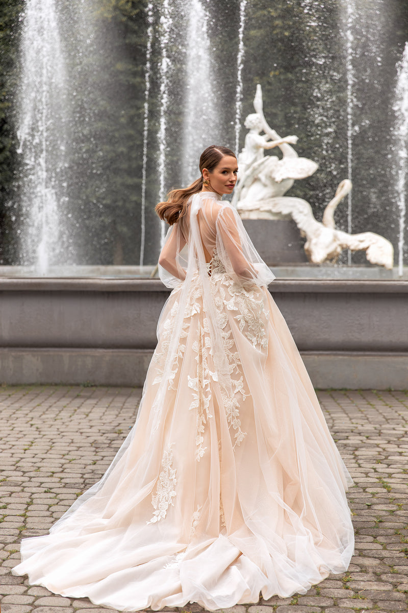 Back view of a cappuccino wedding dress with sheer sleeves, lace appliqués, flowing skirt, and a long train