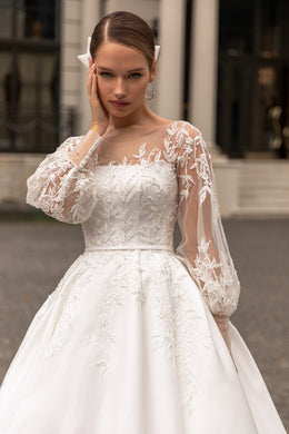 Close-up of an ivory wedding dress with floral lace embroidery, a straight neckline, and sheer long sleeves