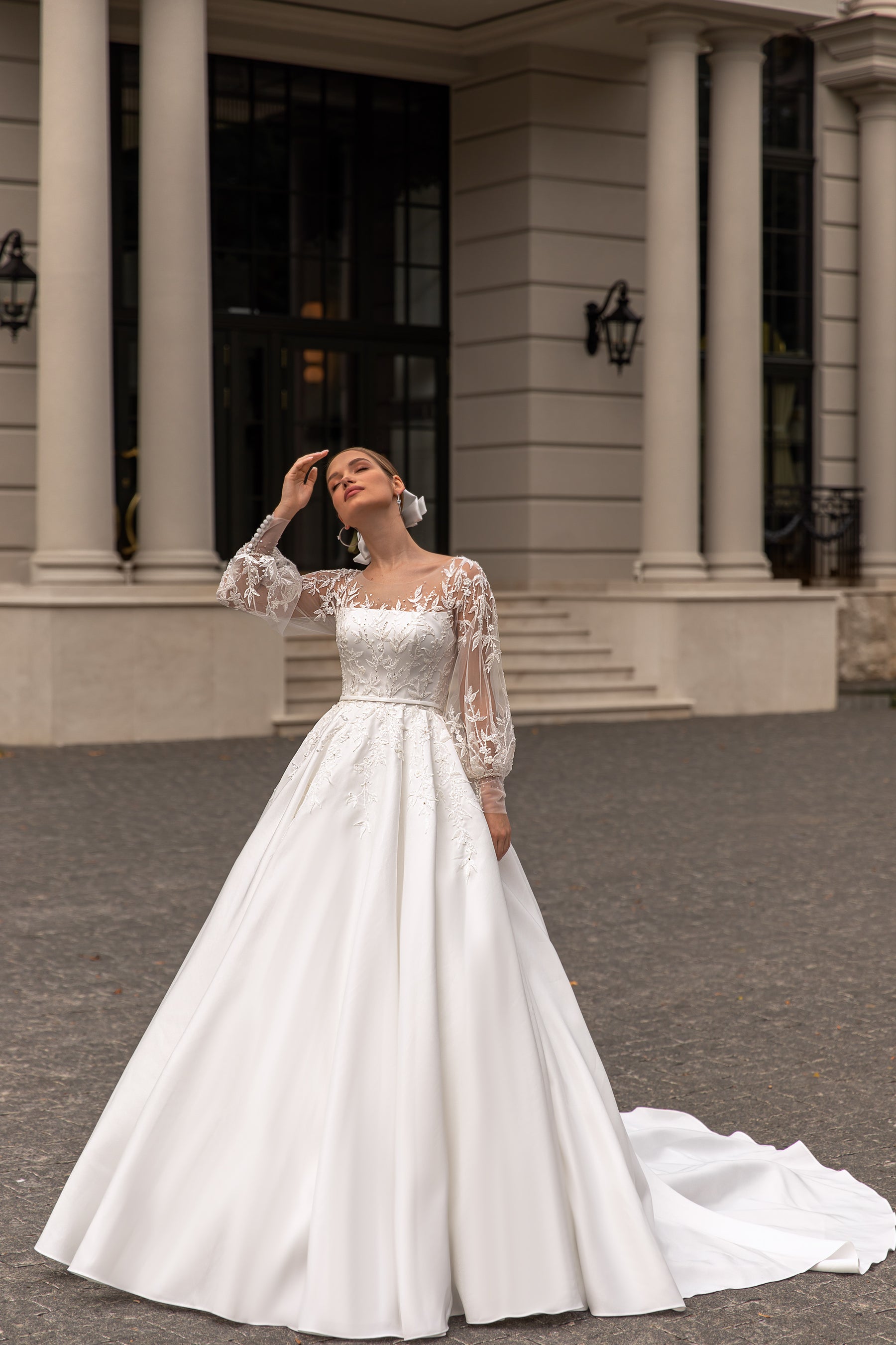 Ivory wedding dress with long lace sleeves, floral bodice appliqués, a full A-line skirt, and a train