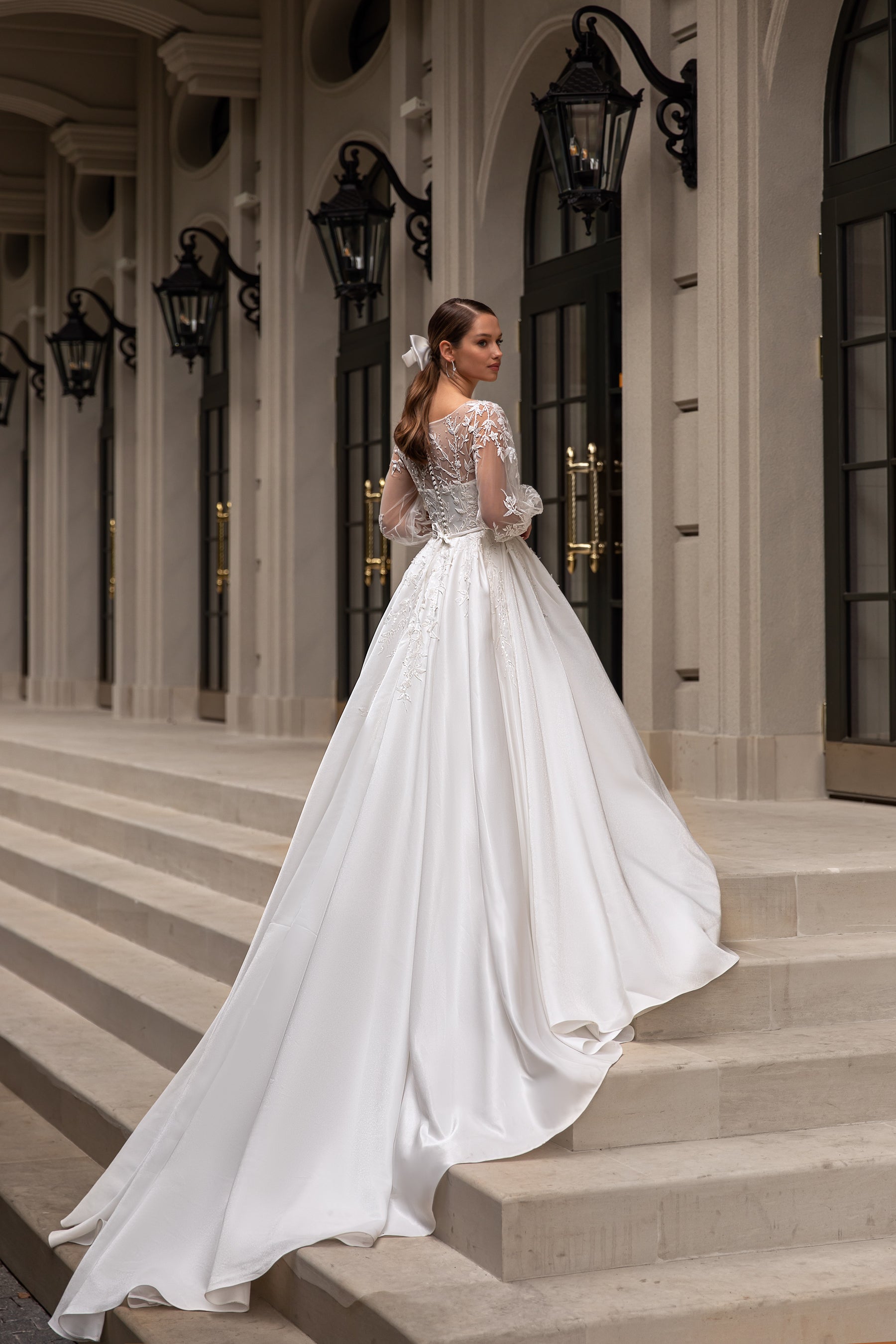 Back view of an ivory wedding dress with a sheer lace back, long sleeves, and an extended train