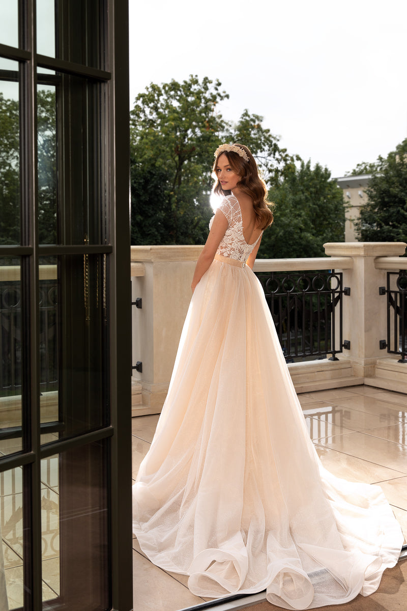 Open lace back and sweeping train on an ivory wedding dress with a sheer, flowing overskirt