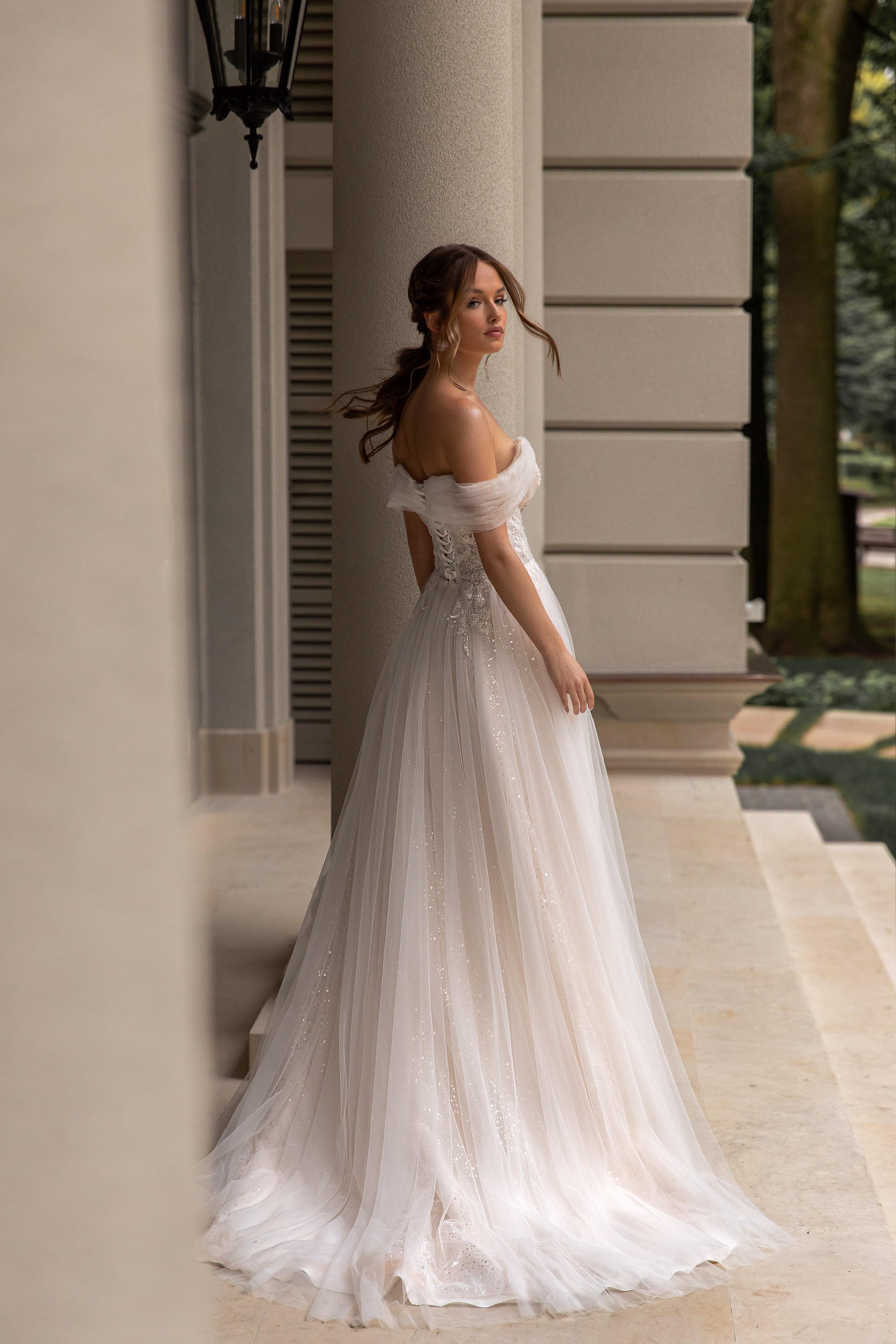 Flowing ivory wedding dress with off-the-shoulder sleeves, a sparkling tulle A-line skirt, and sweeping train