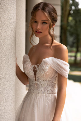 Close-up of an ivory wedding dress bodice with floral lace, beadwork, sweetheart neckline, and sheer sleeves