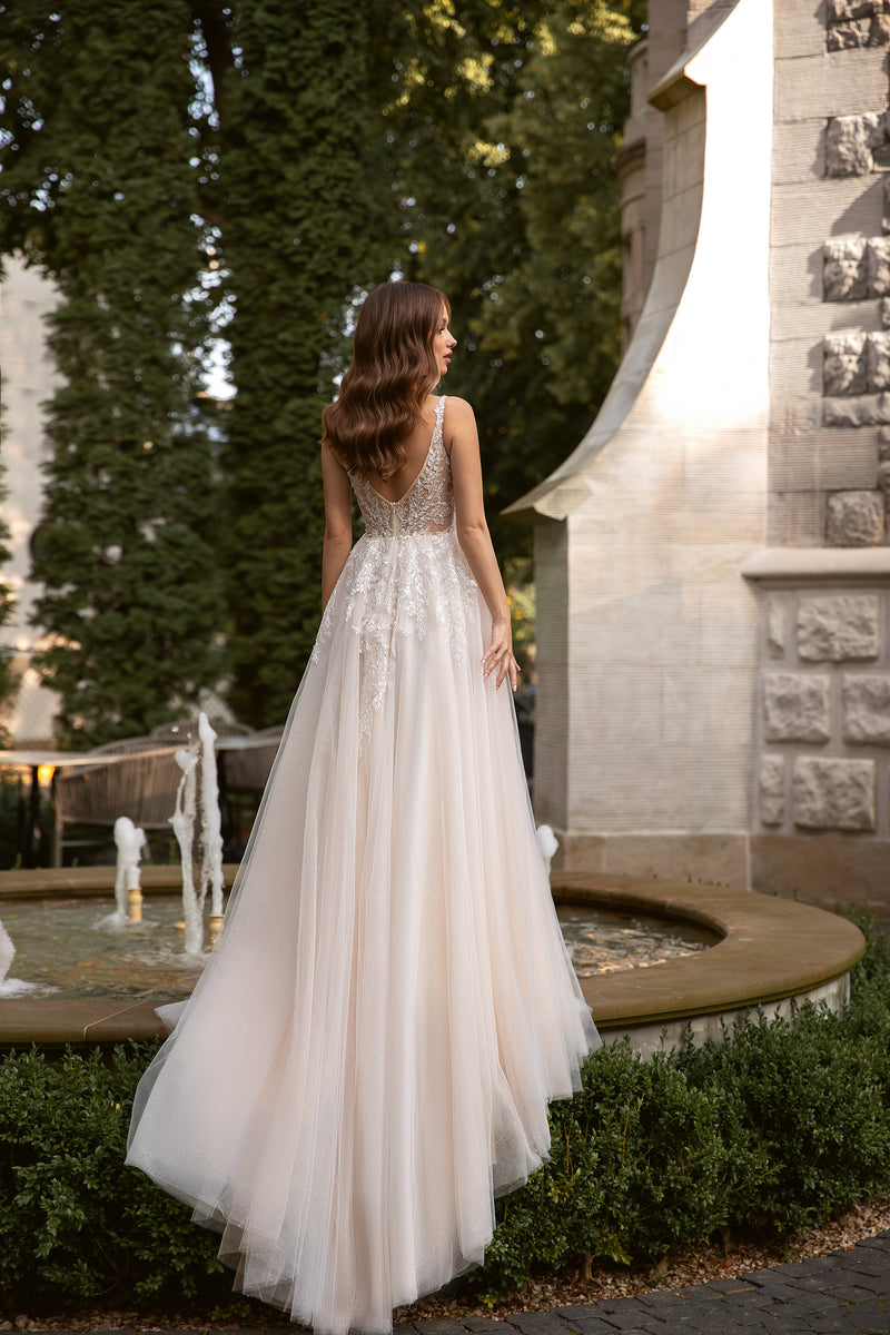 Open V-back wedding dress with lace detailing, thin straps, and a flowing floor-length train