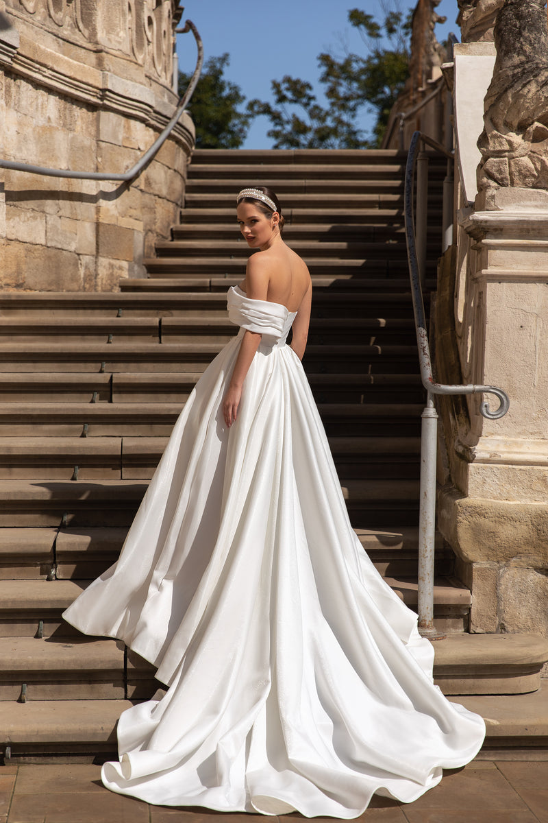 Ivory wedding dress with an open back, off-shoulder draped sleeves, full A-line skirt, and sweeping train