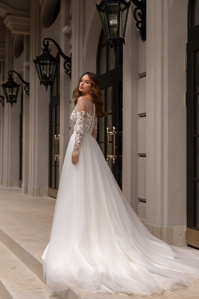 Ivory wedding dress showing a lace-covered back, sheer sleeves, full skirt, and long trailing train