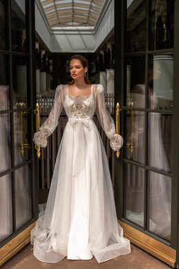 Ivory wedding dress with a beaded bodice, sheer long sleeves, bow waist, and flowing train